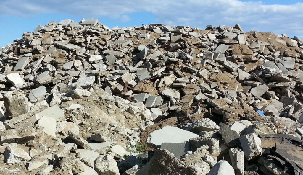 A large pile of broken concrete rubble and debris under a partly cloudy sky, representing the groundwork of a local campaign
