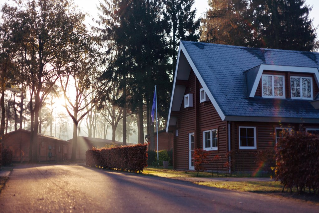 Wooden cabin style house with a steep roof among trees at sunrise, warm brown and green tones, evoking a neighborhood polling day feel