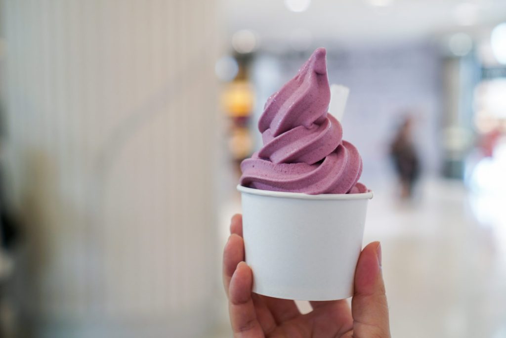 Hand holding a small cup of purple soft-serve dessert with a blurred bright background, a lighter moment from campaign life